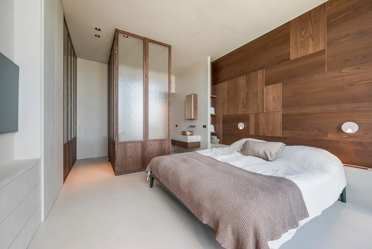 Quarto com parede de madeira na cabeceira e divisória de vidro texturado para a casa de banho