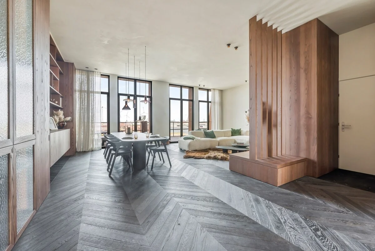 Bright living and dining area with tall windows, sofa and herringbone floor